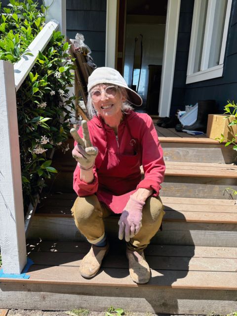 Photo of Sandra Dean in construction worker clothes on back porch, July 2023, by David Bilides
