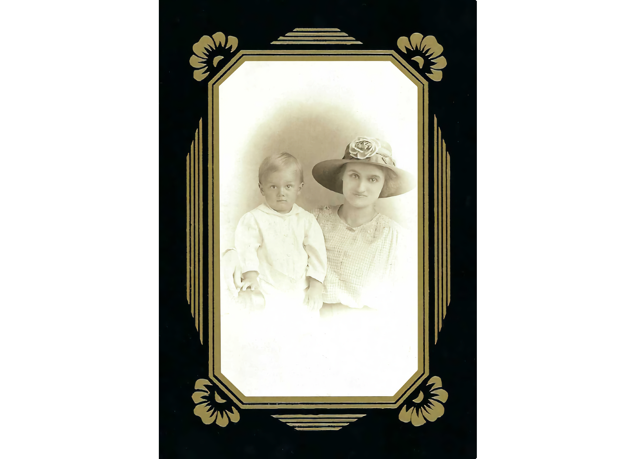 Photo of woman with broad-rimmed hat with boy in white smock on her right, in a black and gold frame.