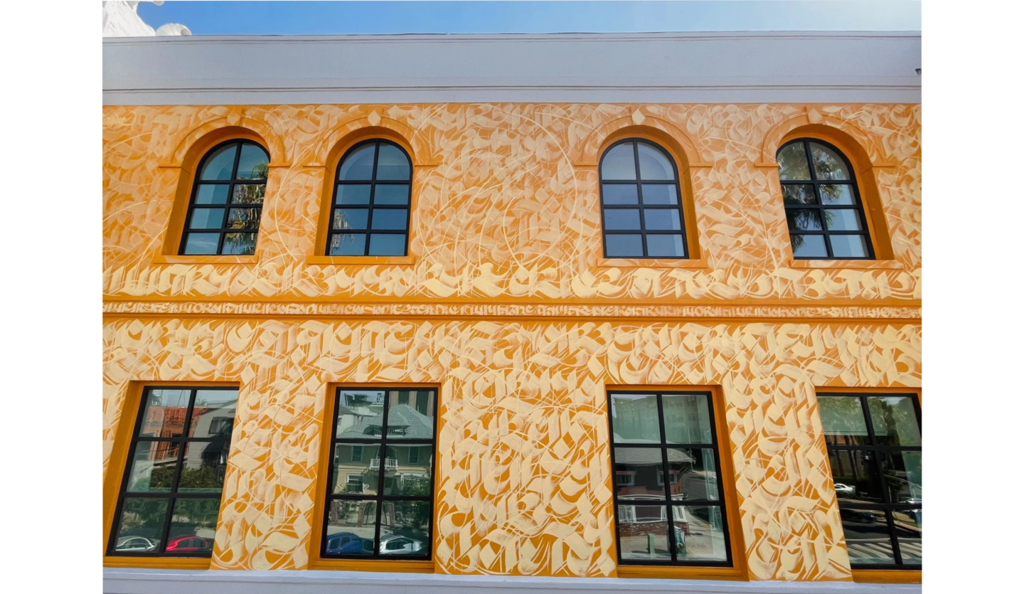 Photo ofwall of 2-story building with 4 arched windows on top and 4 rectangular windows on bottom, with wall decorated with golden calligraphy on orange background