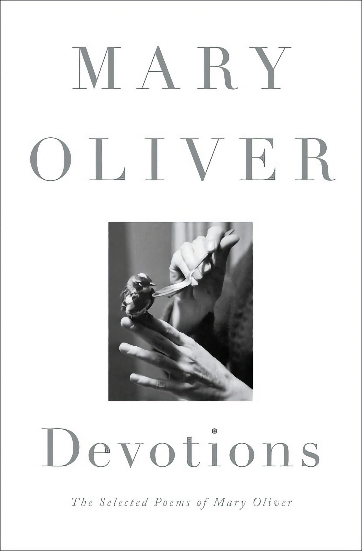 Image of book Devotions, by Mary Oliver, with photo of hand feeding small bird.
